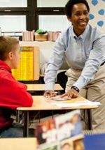 Loretta leaning over a desk to talk with a student in a classroom