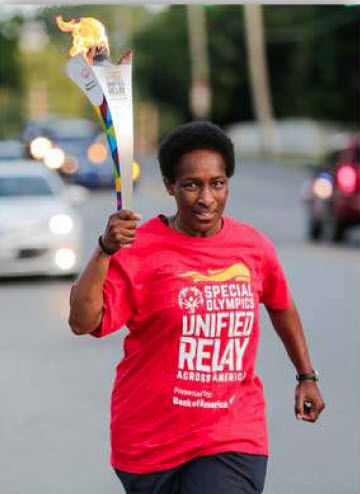 Loretta carrying a torch in a red Special Olympics Unified Relay Across America shirt