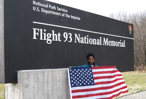 Loretta holding a U.S. flag beside the Flight 93 National Memorial sign