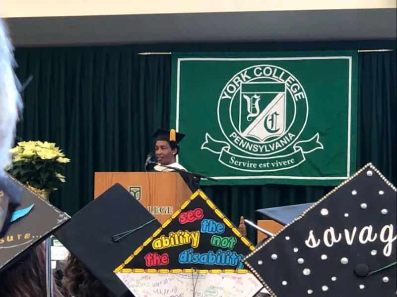 Loretta speaking at a York College commencement, seen past graduates' decorated caps