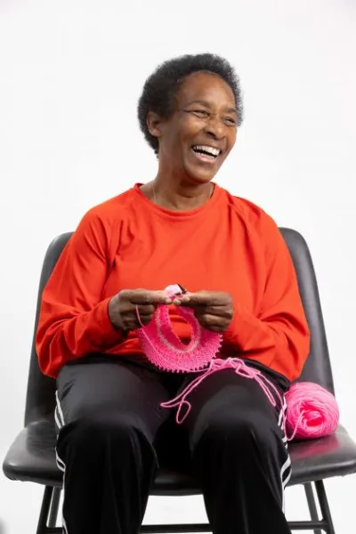 Loretta laughing as she knits with pink yarn