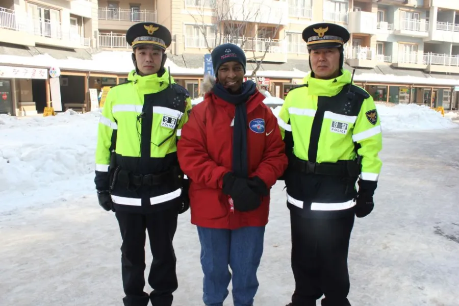 Loretta standing between two police officers in high-visibility jackets in the snow