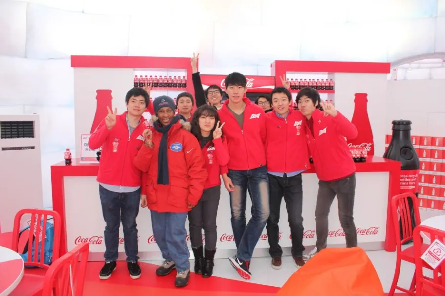 Loretta posing with a group of young people in red jackets at a Coca-Cola stand